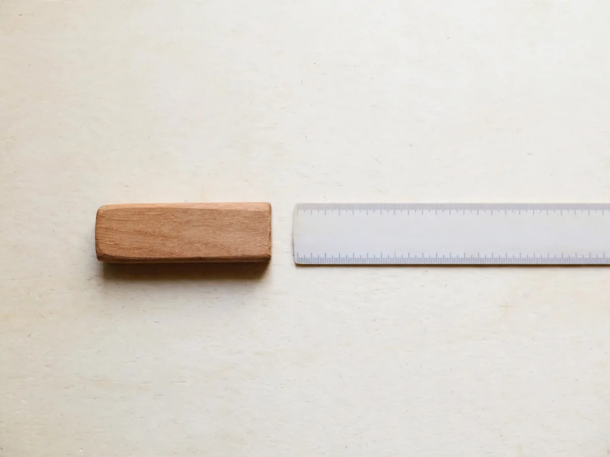 A small wooden object beside a ruler on a flat surface, photographed from directly above.